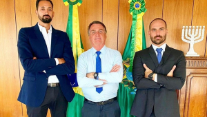 Maurício Souza (à esquerda, de terno e gravata), Jair Bolsonaro (no meio, de camisa, gravata azul e calça social) e Eduardo Bolsonaro (à direita, de terno e gravata) posam para foto no Palácio do Planalto, todos de braços cruzados