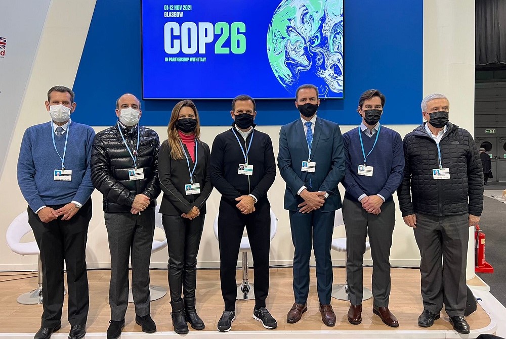 Perfilado com outras seis autoridades que participaram com ele de painel sobre mudanças climáticas (três à sua esquerda e três à sua direita), João Doria posa para foto em frente a uma tela com o símbolo da COP26