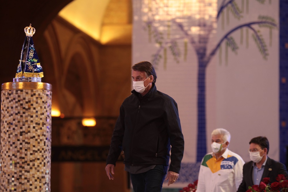 De máscara, calça jeans e jaqueta, Jair Bolsonaro caminha pelo Santuário de Aparecida e observa a imagem de Nossa Senhora, que está em um altar