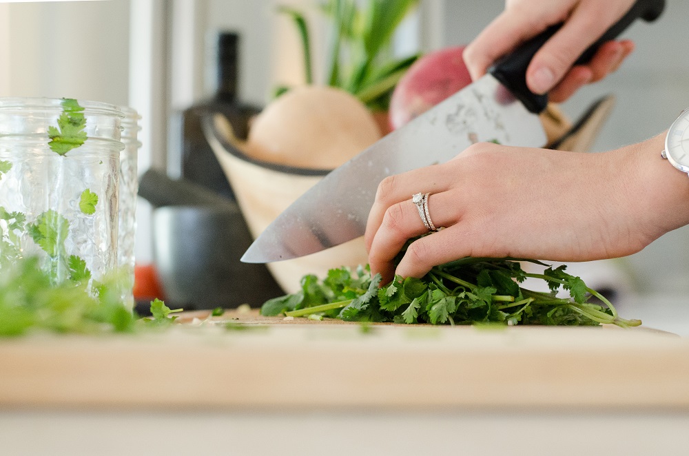 Mão com uma faca corta salada em uma tábua na cozinha