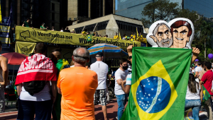 Boneco do Lula e de Bolsonaro juntos, parcialmente encobertos pela bandeira do Brasil, durante manifestação contra Bolsonaro na avenida Paulista