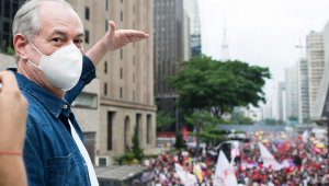 Do alto de um trio elétrico na Avenida Paulista, Ciro Gomes estica o braço esquerdo para sinalizar altura, enquanto manifestantes, alguns com bandeiras e faixas, protestam contra Bolsonaro no asfalto