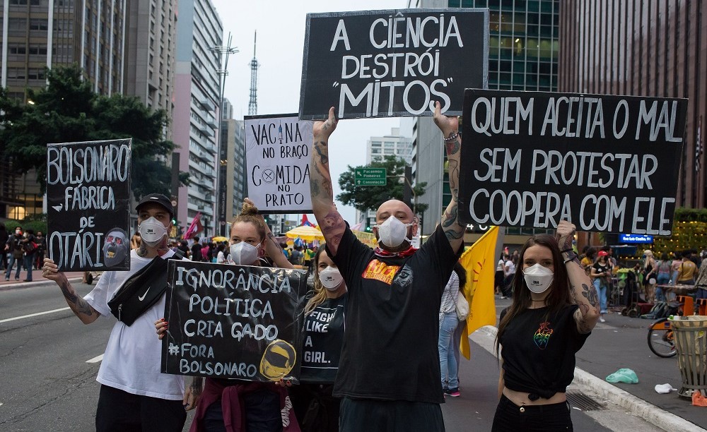 Cinco jovens manifestantes (dois homens e três mulheres), todos de preto, levantam cartazes contra Bolsonaro na Avenida Paulista