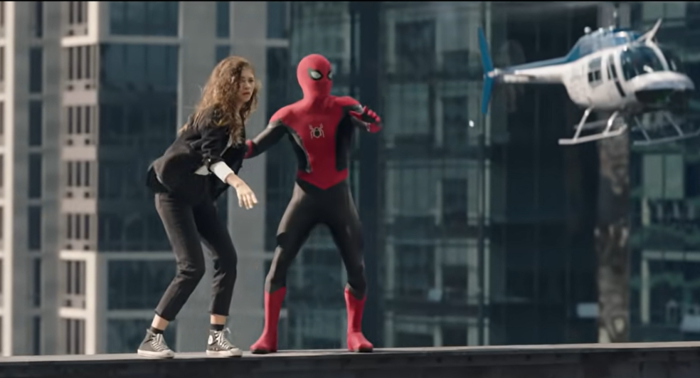 O Homem Aranha segura MJ pelo braço, e os dois se equilibram em uma plataforma a muitos metros de altura, enquanto um helicóptero passa perto deles