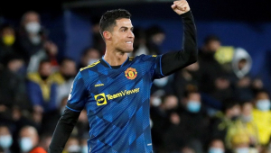 Cristiano Ronaldo, com o uniforme azu escuro do Manchester United, levanta o braço esquerdo e sorri após marcar um gol