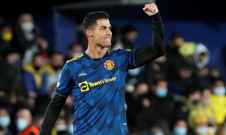 Cristiano Ronaldo, com o uniforme azu escuro do Manchester United, levanta o braço esquerdo e sorri após marcar um gol
