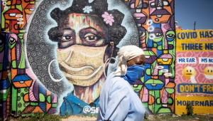 Uma moradora do bairro de Soweto, em Joanesburgo, África do Sul, passa por um mural que retrata uma mulher usando uma máscara