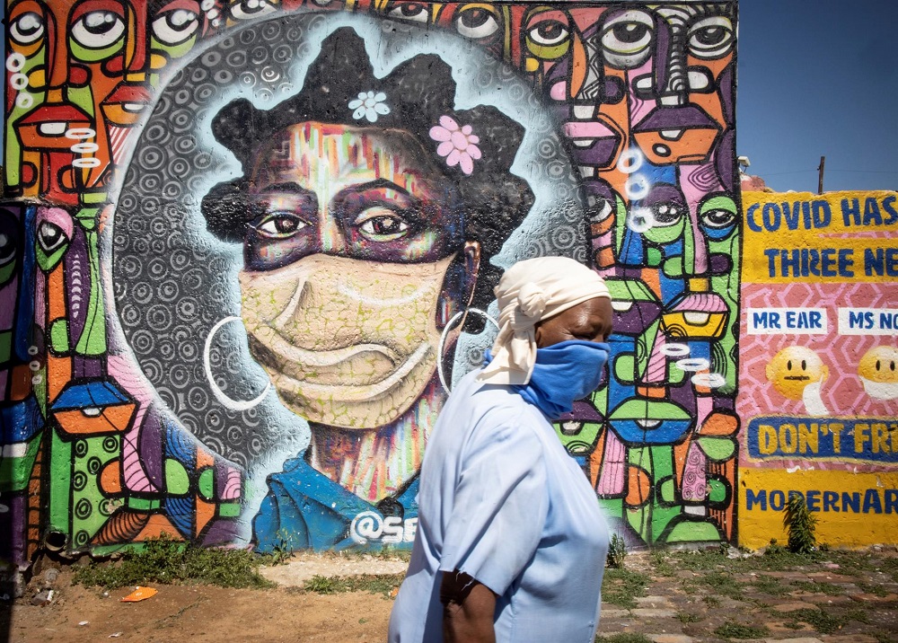 Uma moradora do bairro de Soweto, em Joanesburgo, África do Sul, passa por um mural que retrata uma mulher usando uma máscara