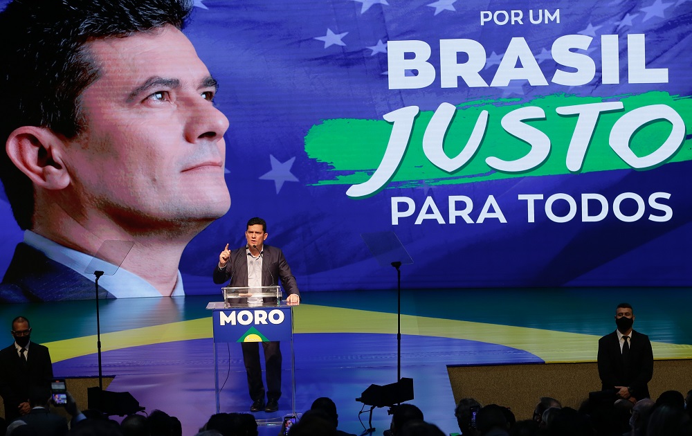 À frente de um púlpito, Sergio Moro discursa em frente a um gigante painel com sua cara e a mensagem 