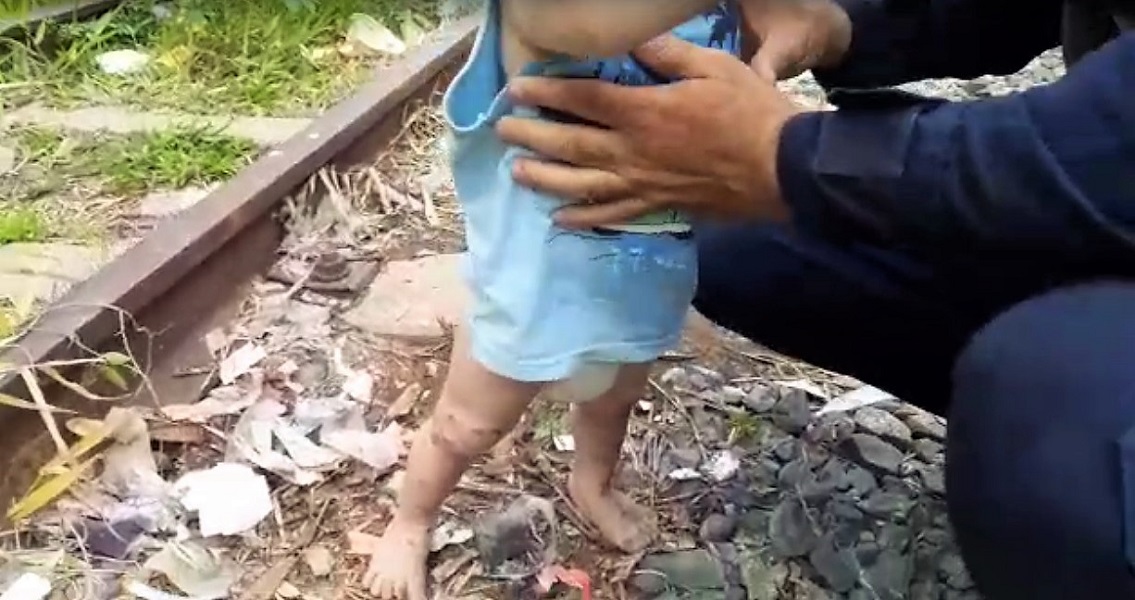 Sem exibir rostos, imagem mostra guarda segurando bebê em linha de trem