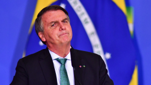O presidente Jair Bolsonaro em frente a uma bandeira do Brasil