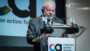 Lula. em trajes sociais, dá entrevista em um púlpito de acrílico num fórum de Madri
