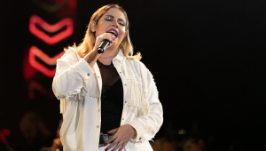 De jaqueta branca camiseta preta e olhos fechados, Marília Mendonça canta no palco