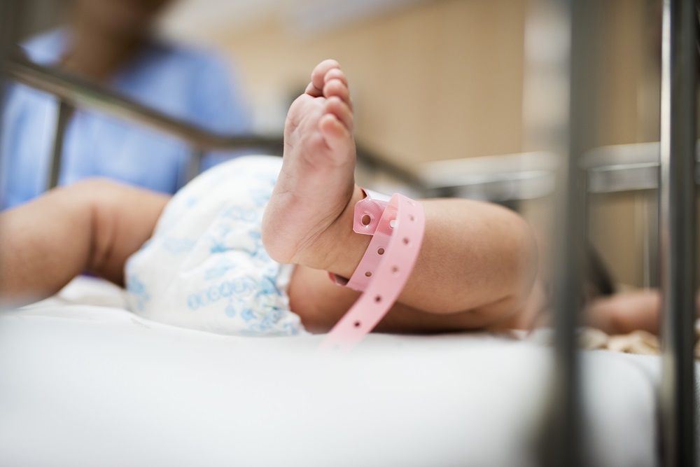 Foto de um berço onde aparece parte de um recém-nascido (o pé direito e a fralda)