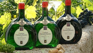 Três vinhos de garrafa ondulada colocados lado a lado em uma mureta, com algumas uvas ao redor