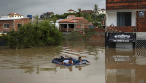 Homens usam bote inflável para atravessar região alagada por chuvas na Bahia