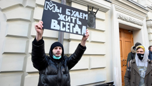 Membro da ONG Memorial segura placa em russo com dizeres 'Vamos viver para sempre' em protesto à dissolução do órgão