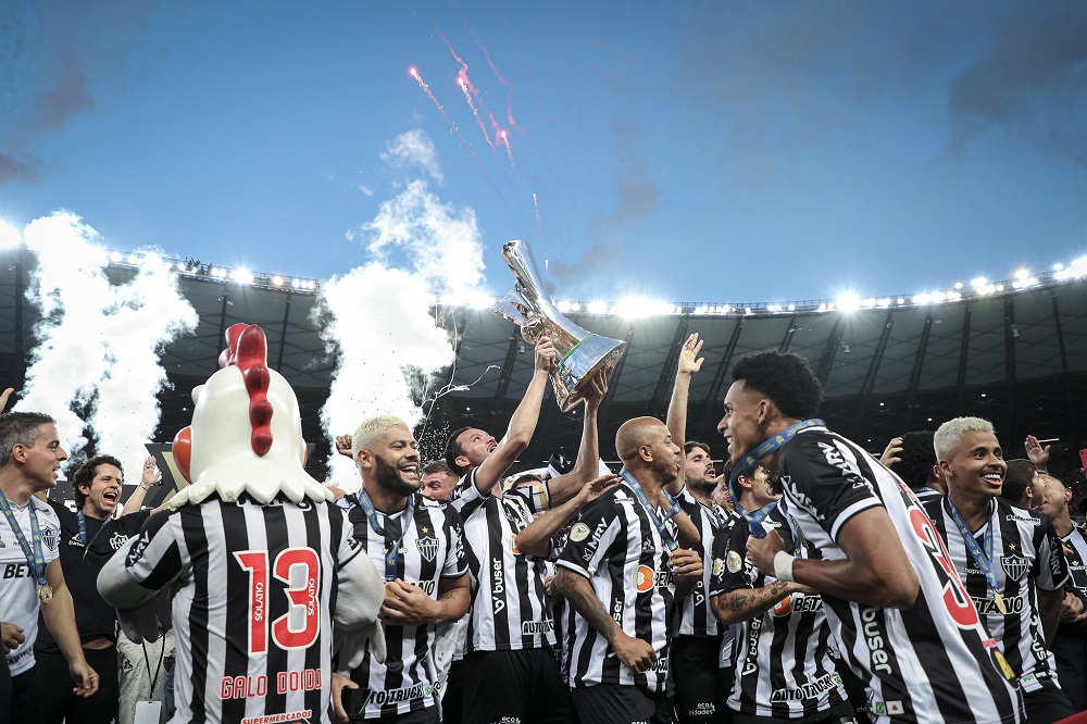 Amontoados, com o uniforme alvinegro do clube, jogadores do Atlético-MG comemoram o título em campo, com Réver erguendo a taça e participação até do mascote