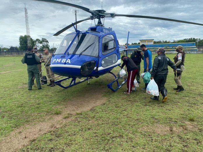Pessoas retiram cestas básicas de helicóptero em campo gramado