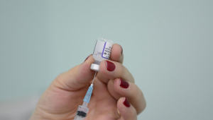 Mão feminina segura frasco de vacina e coloca agulha