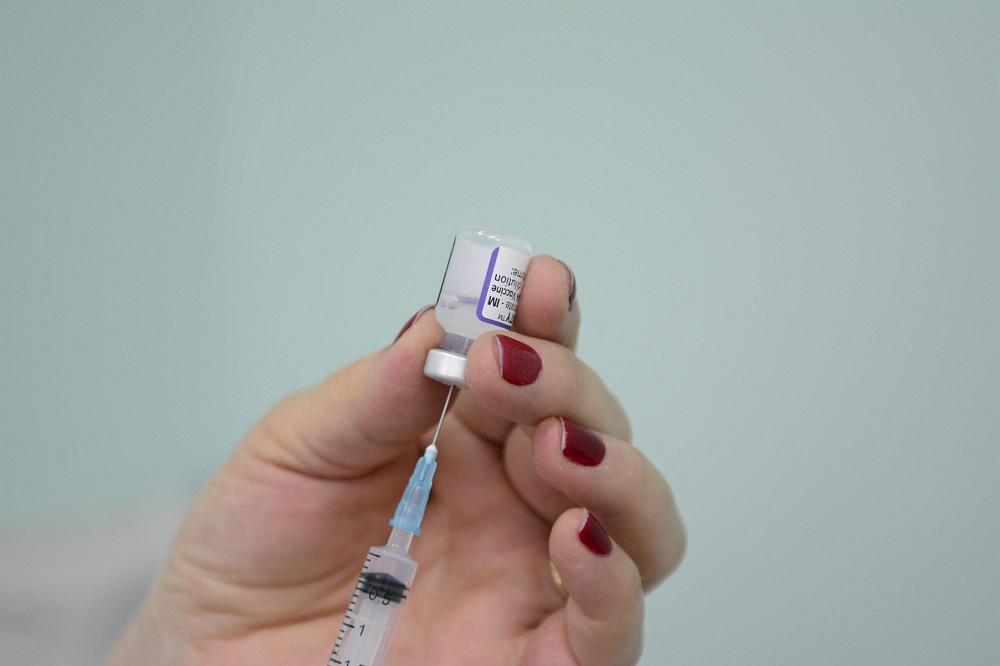 Mão feminina segura frasco de vacina e coloca agulha