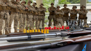 Dez homens em trajes camuflados posam atrás de armas e munições apreendidas