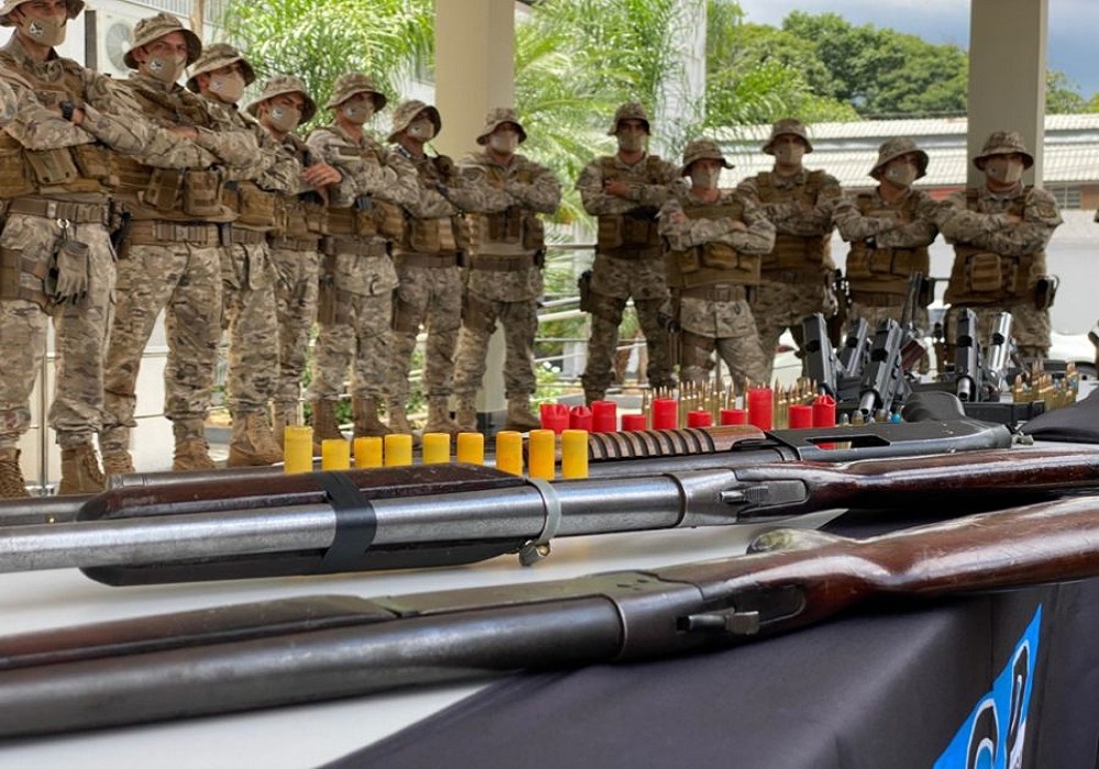 Dez homens em trajes camuflados posam atrás de armas e munições apreendidas