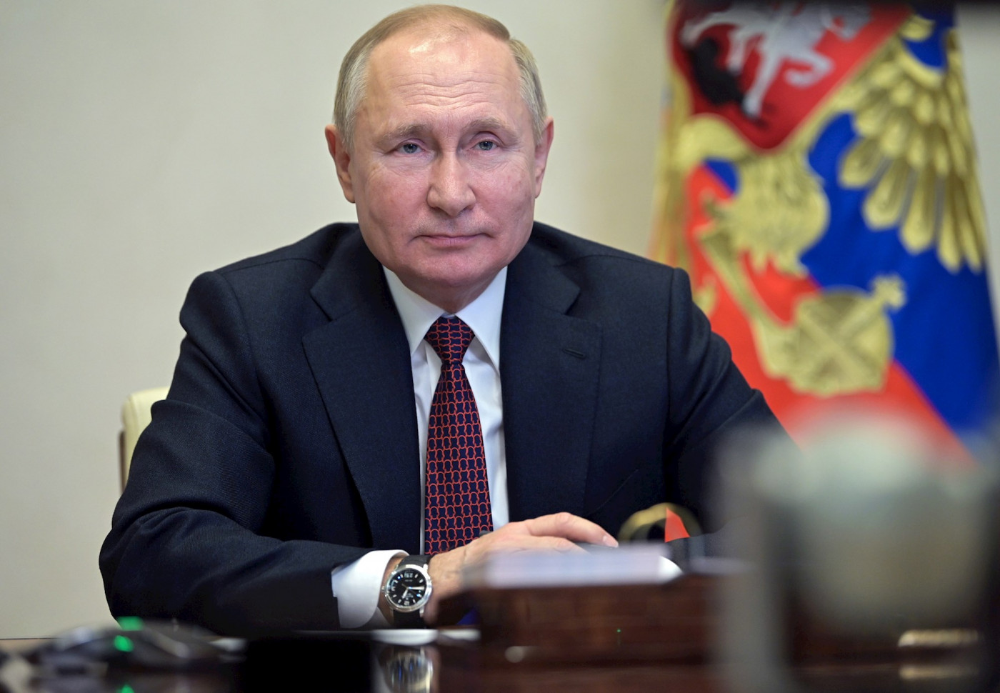 Vladimir Putin de terno e gravata, com bandeira ao fundo