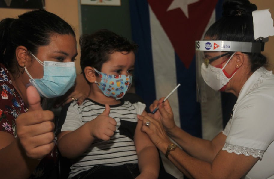 Crianças ao lado da mãe recebendo vacina contra a Covid-19 por uma enfermeira