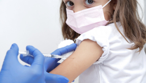 Mão de uma nefermeira com luva aplicando vacina em uma criança