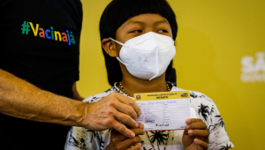 menino indígena segurando comprovante de vacinação