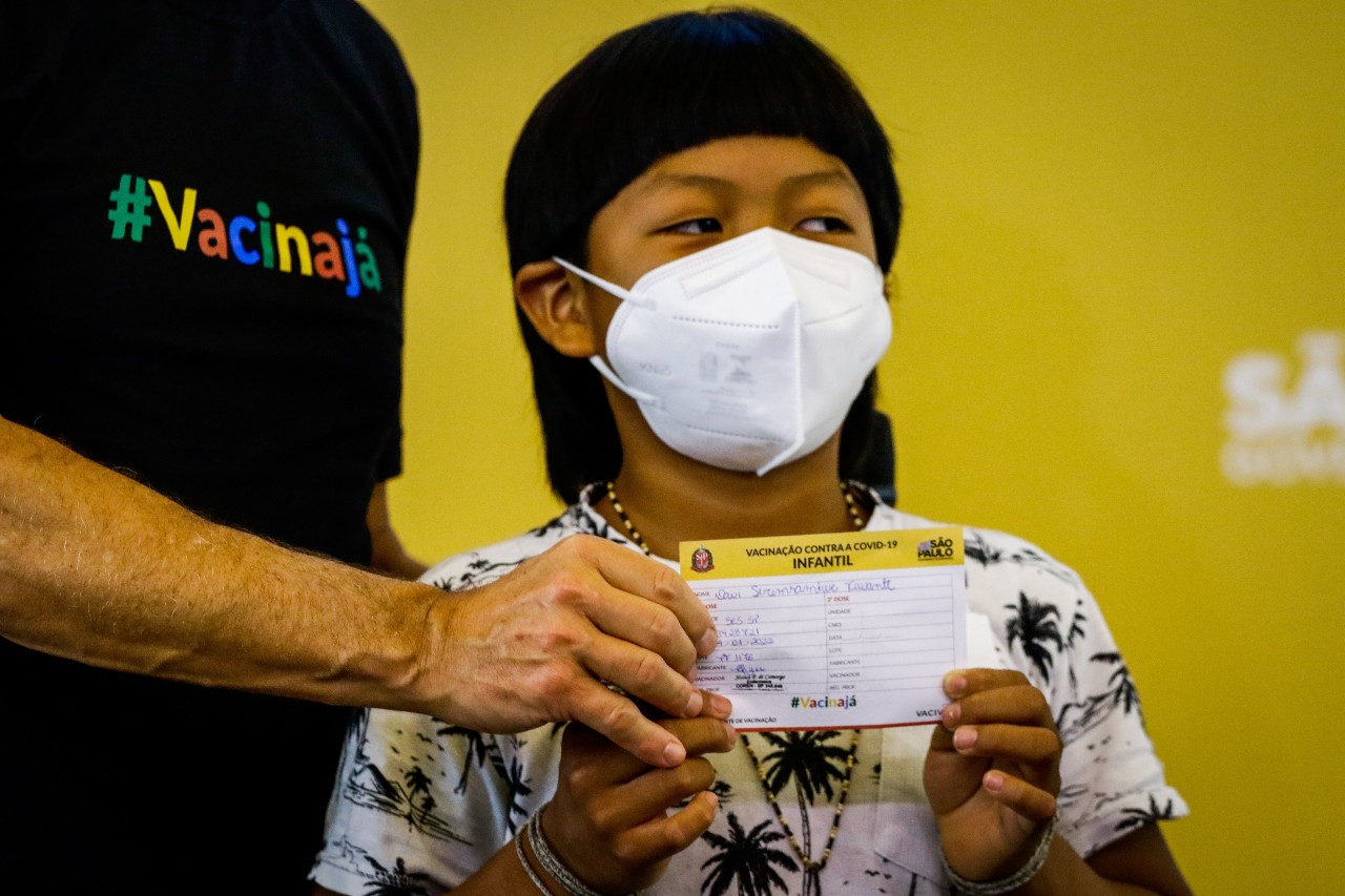 menino indígena segurando comprovante de vacinação