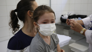 Criança com máscara no colo da mãe esperando para ser vacinada contra a Covid-19