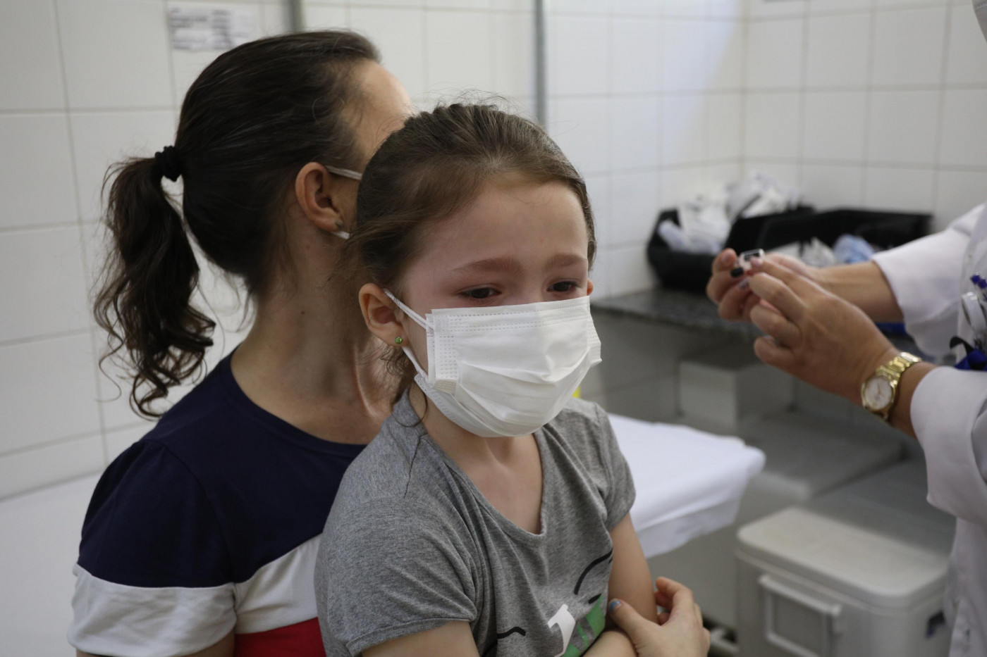 Criança com máscara no colo da mãe esperando para ser vacinada contra a Covid-19