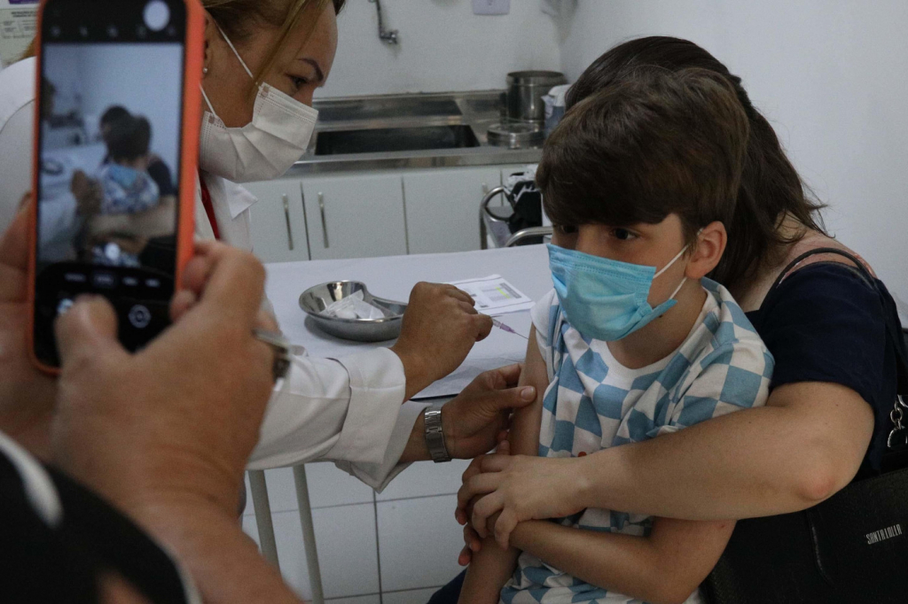 Mão segura celular para tirar foto de criança sendo imunizada