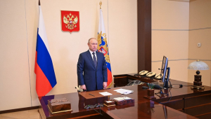 Putin em sala do Kremlin, ao lado de bandeiras da Rússia