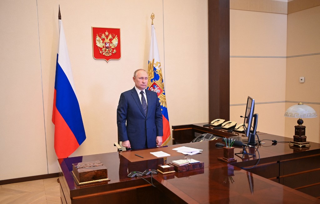 Putin em sala do Kremlin, ao lado de bandeiras da Rússia