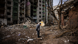 Homem olha para o chão ao redor de prédios destruídos na guerra na Ucrânia