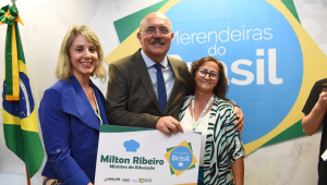 O ministro Milton Ribeiro entre duas mulheres, sendo que uma delas o ajuda a segurar uma paca com seu nome e cargo, durante lançamento de um reality show promovido pela pasta