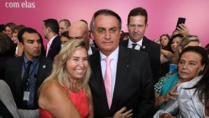 Rodeado de jornalistas e fãs, Jair Bolsonaro é abraçado por uma mulher em um evento de celebração ao Dia Internacional da Mulher