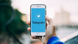Mão com celular mostra tela de início do Telegram