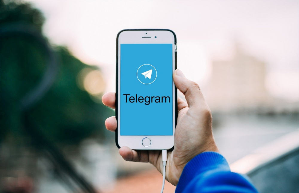 Mão com celular mostra tela de início do Telegram