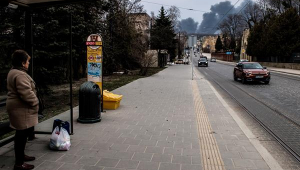 Pessoa em ponto de ônibus observa fumaça após ataque aéreo