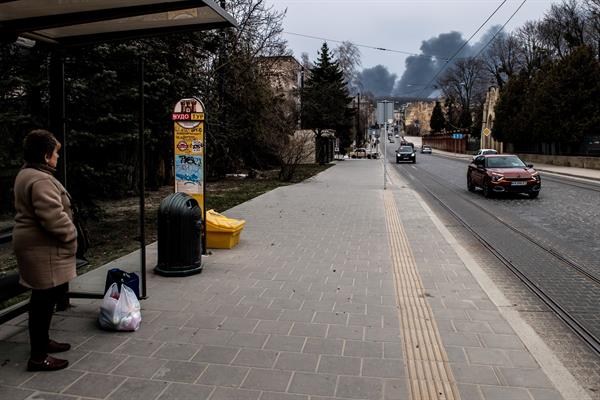 Pessoa em ponto de ônibus observa fumaça após ataque aéreo