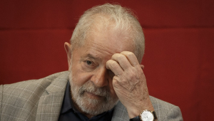 Sentado, de paletó xadrez e camiseta preta, Lula coça a testa com a mão esquerda