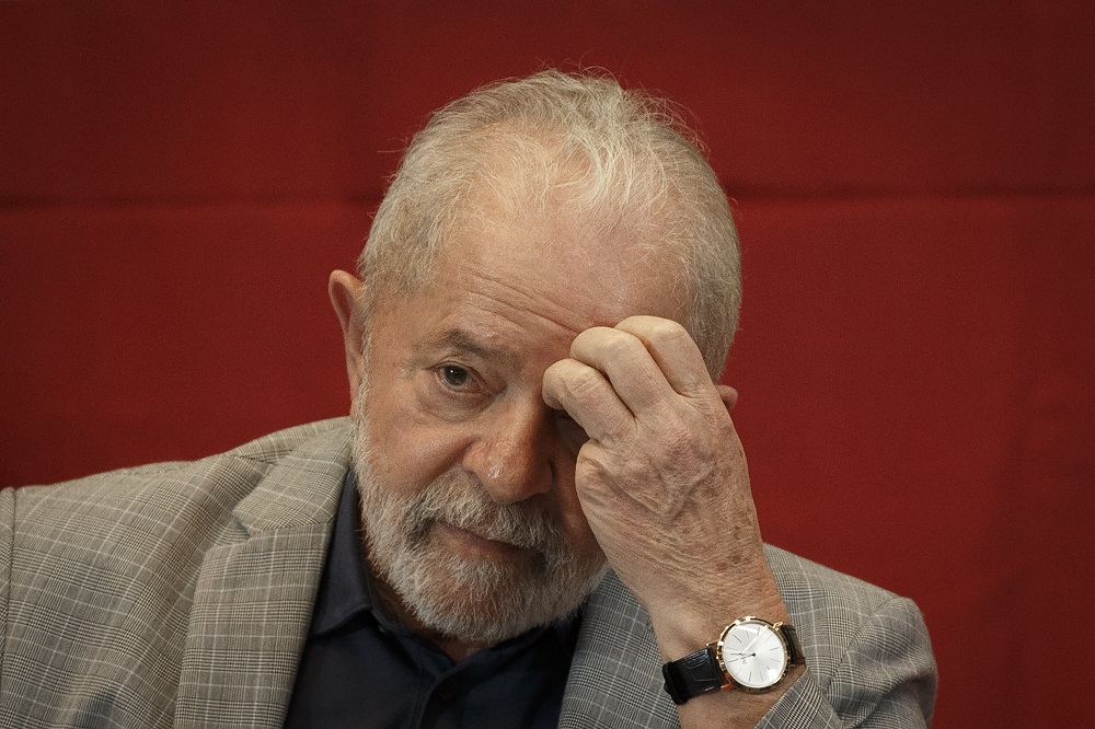 Sentado, de paletó xadrez e camiseta preta, Lula coça a testa com a mão esquerda