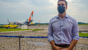 Eduardo Leite, de camisa,, calça social e máscara, se posiciona à frente de uma pista de pouso, com um avião estacionado