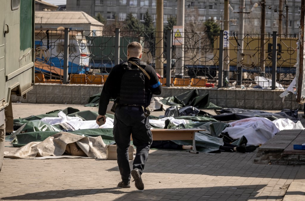 Policial ucraniano caminha em direção a corpos cobertos com folhas de plástico após bombardeio em estação de trem em Kramatorsk