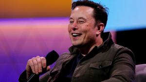 Elon MUsk sorrindo enquanto fala com platéria. Ele segura um microdofone
