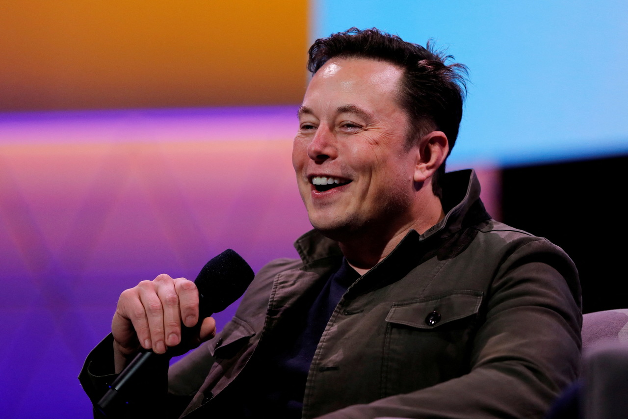 Elon MUsk sorrindo enquanto fala com platéria. Ele segura um microdofone